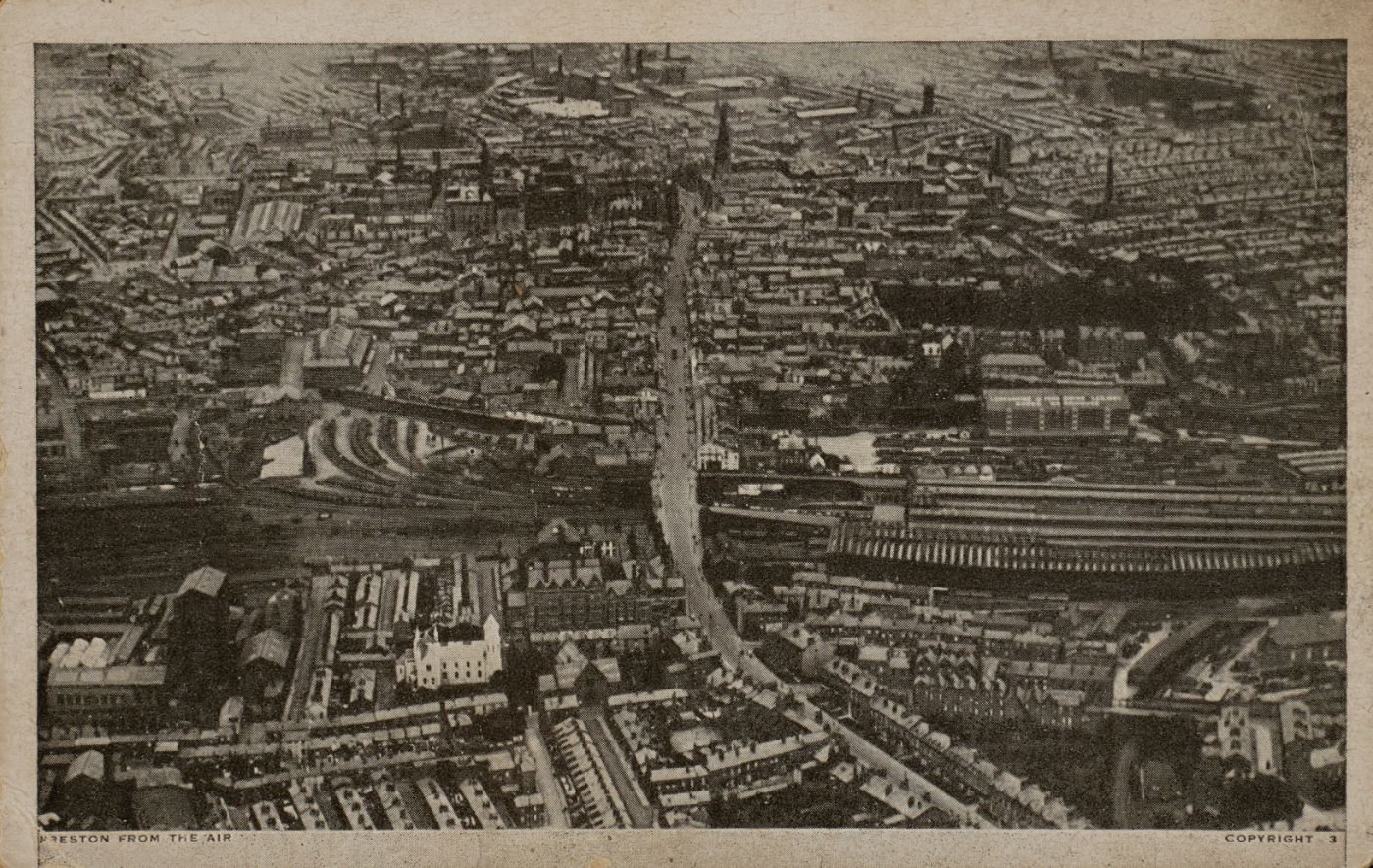 Printed postcard of Preston seen from the air, dense terraced streets and a railway station and sidings running across the middle distance, captioned "Preston from the Air."
