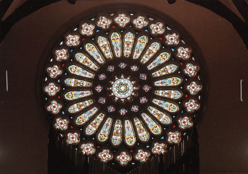 Colour photograph of St Walburge's rose window seen from inside the church, its stained glass petals lit from behind against the dark stone tracery.