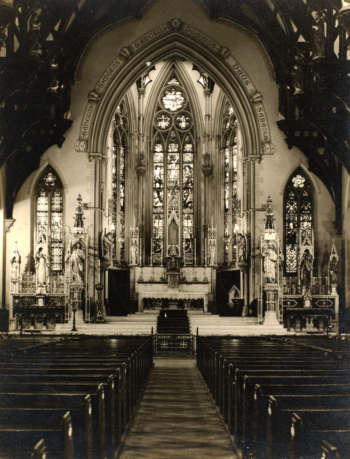 Photograph of St Walburge's sanctuary and great east window seen down the empty nave, side altars either side, pews in the foreground.