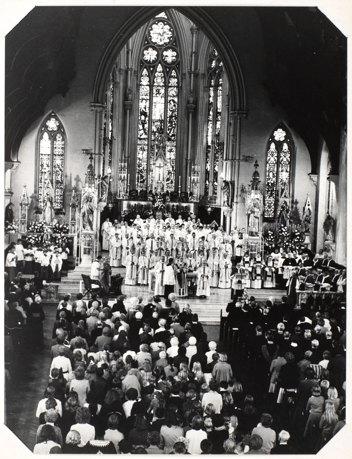 Photograph of Mass at St Walburge's, many priests in white vestments filling the sanctuary before the great east window, a full congregation standing at the pews.
