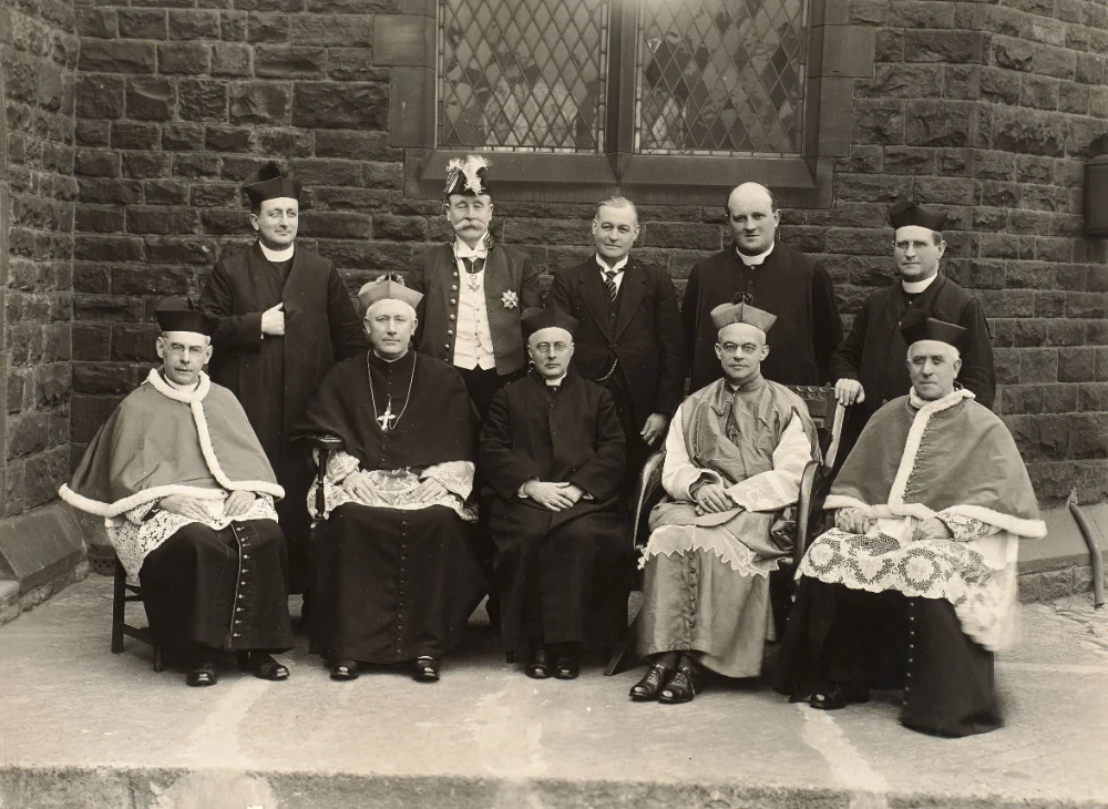 Clergy and one layman stand and sit for a group photograph outside the church.