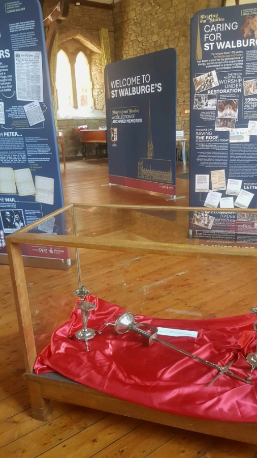 Glass display case of items on red satin in front of "Sharing our Stories" exhibition banners at St Walburge's.