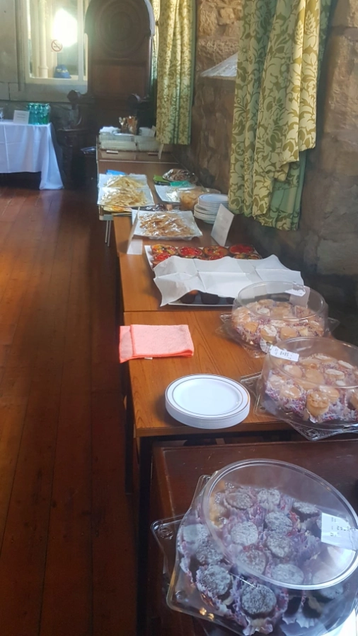 A long table in the hall laid out with refreshments for the Exhibition launch event, including plates of sandwiches and pastries, cupcakes and cakes.